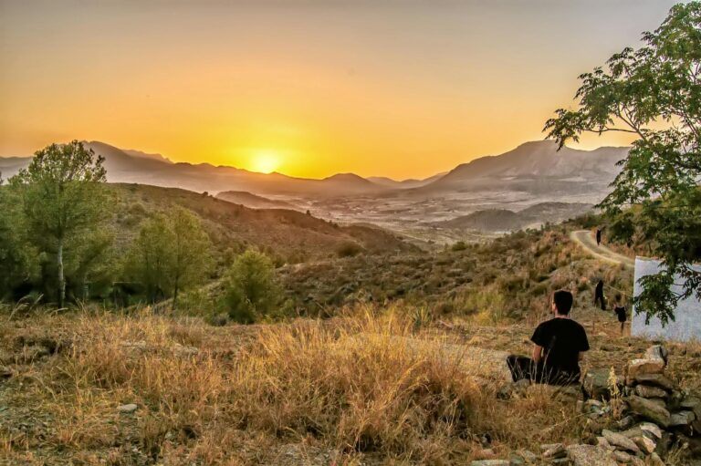 Peaceful sunset view over mountainous terrain with a person relaxing, capturing nature's beauty.